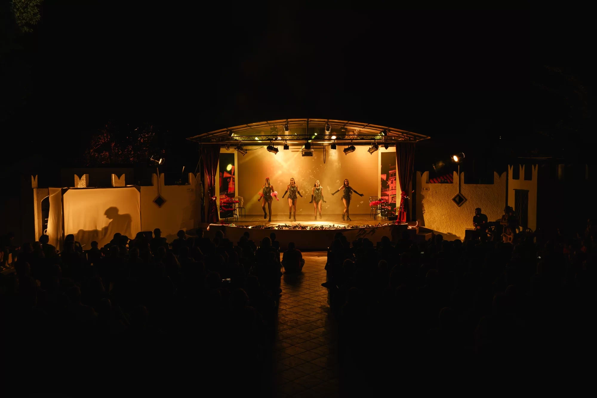 Gruppo di danzatori sul palcoscenico illuminato durante uno spettacolo serale all'aperto.