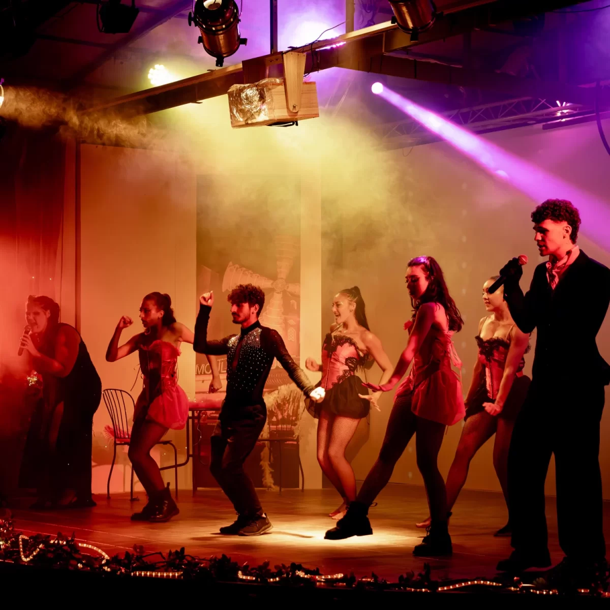 Spettacolo teatrale con ballerini e cantanti sotto luci colorate.