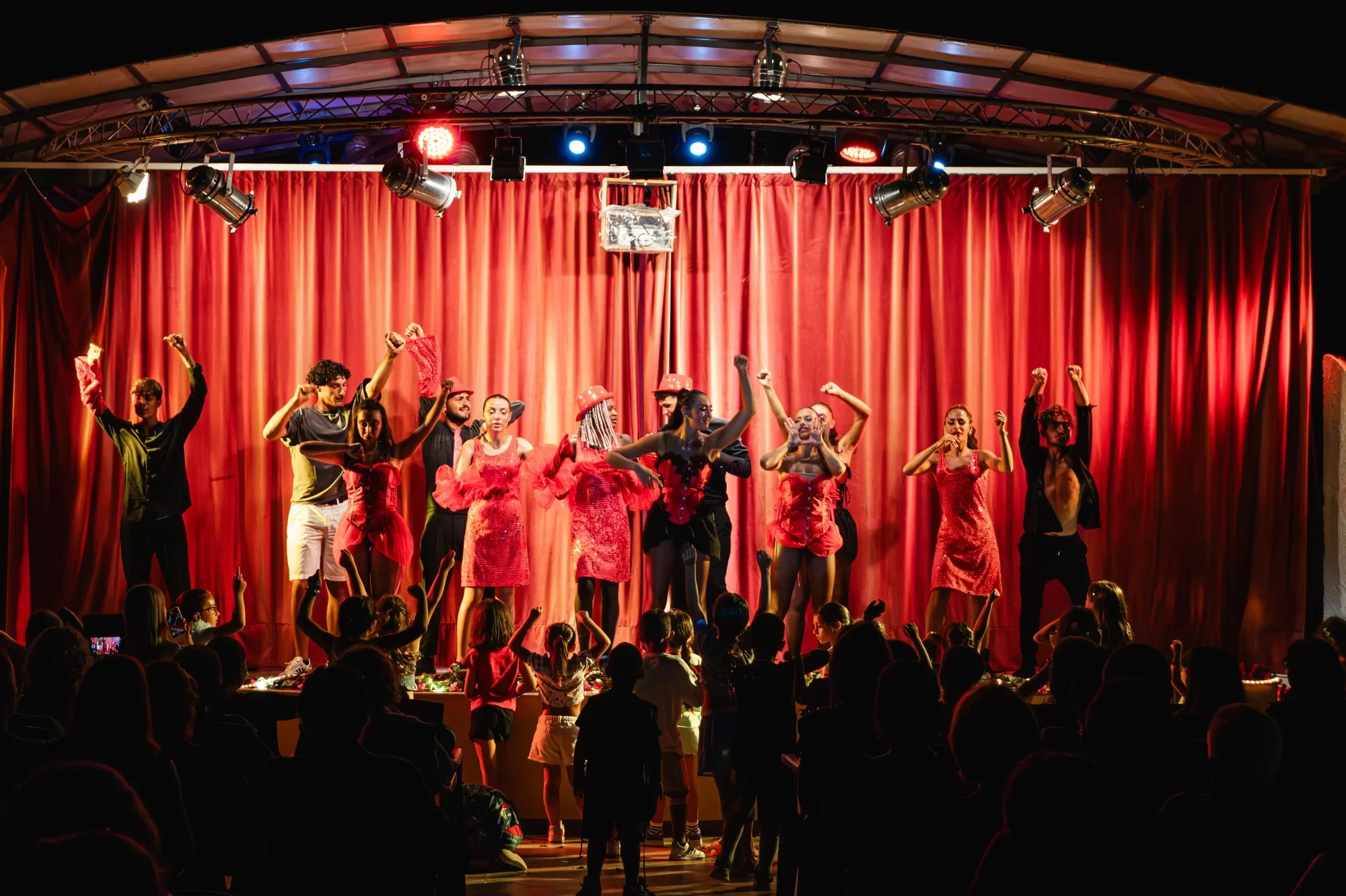 Gruppo di ballerini in costume rosso si esibisce su un palco di fronte a un pubblico entusiasta.
