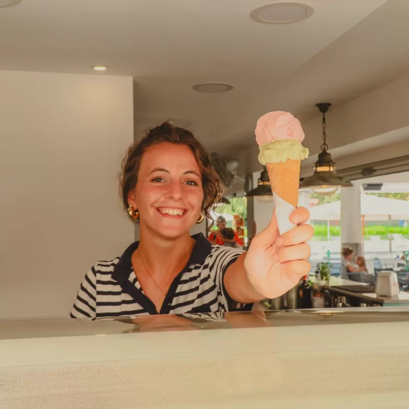 Donna sorridente che serve un cono gelato con due gusti in una gelateria.