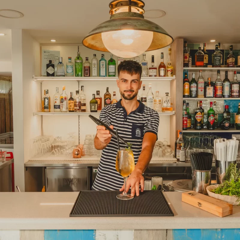 Un barista prepara un cocktail dietro al bancone di un bar ben fornito.