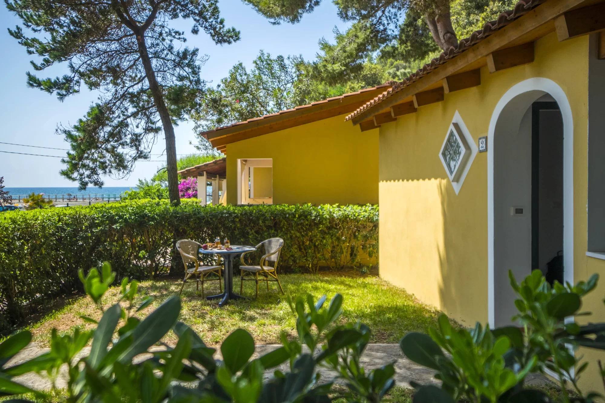 Giardino con tavolo e sedie davanti a una casa gialla in un ambiente balneare.