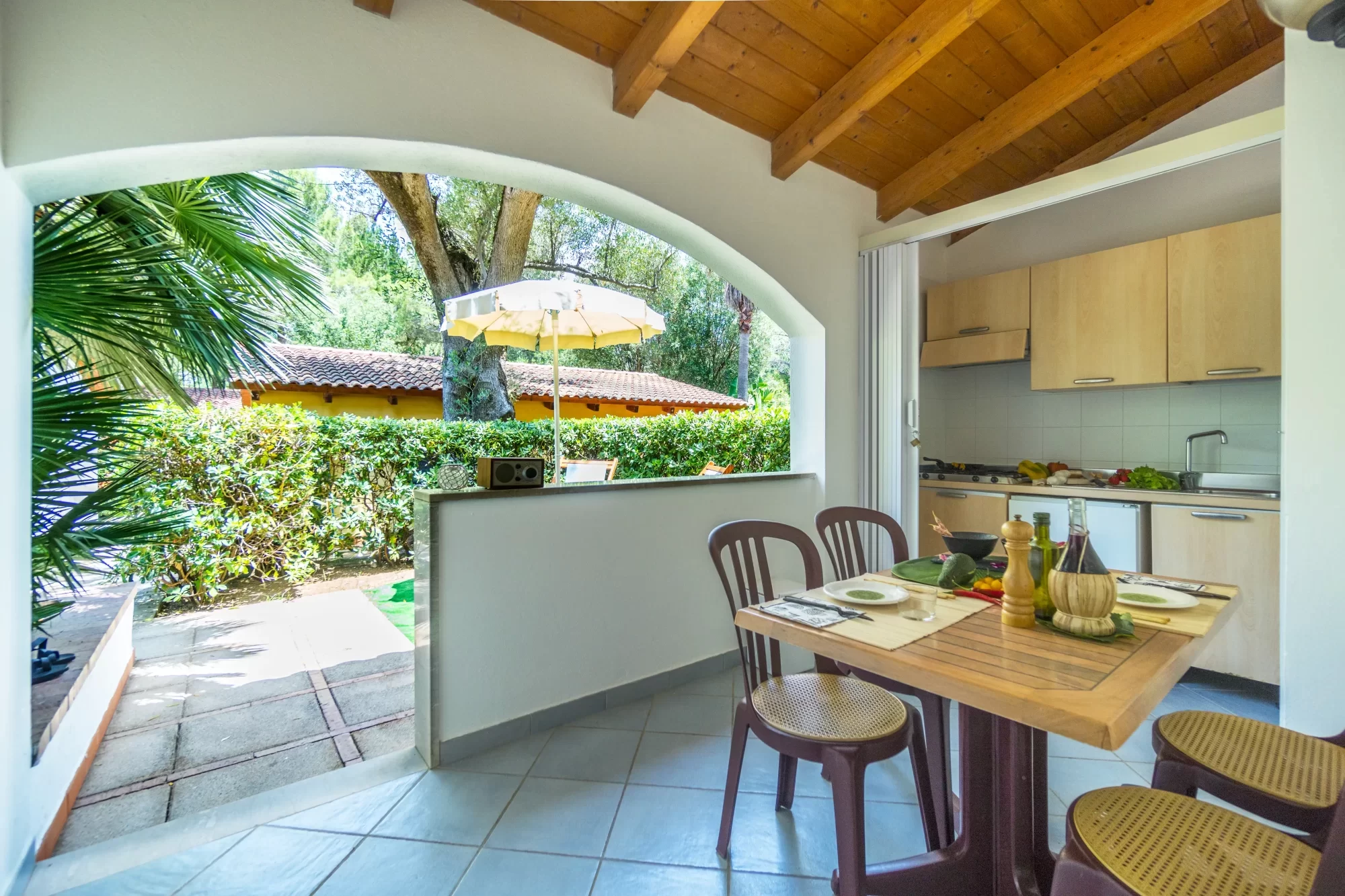 Cucina aperta su un giardino verde con tavolo apparecchiato e vista esterna.
