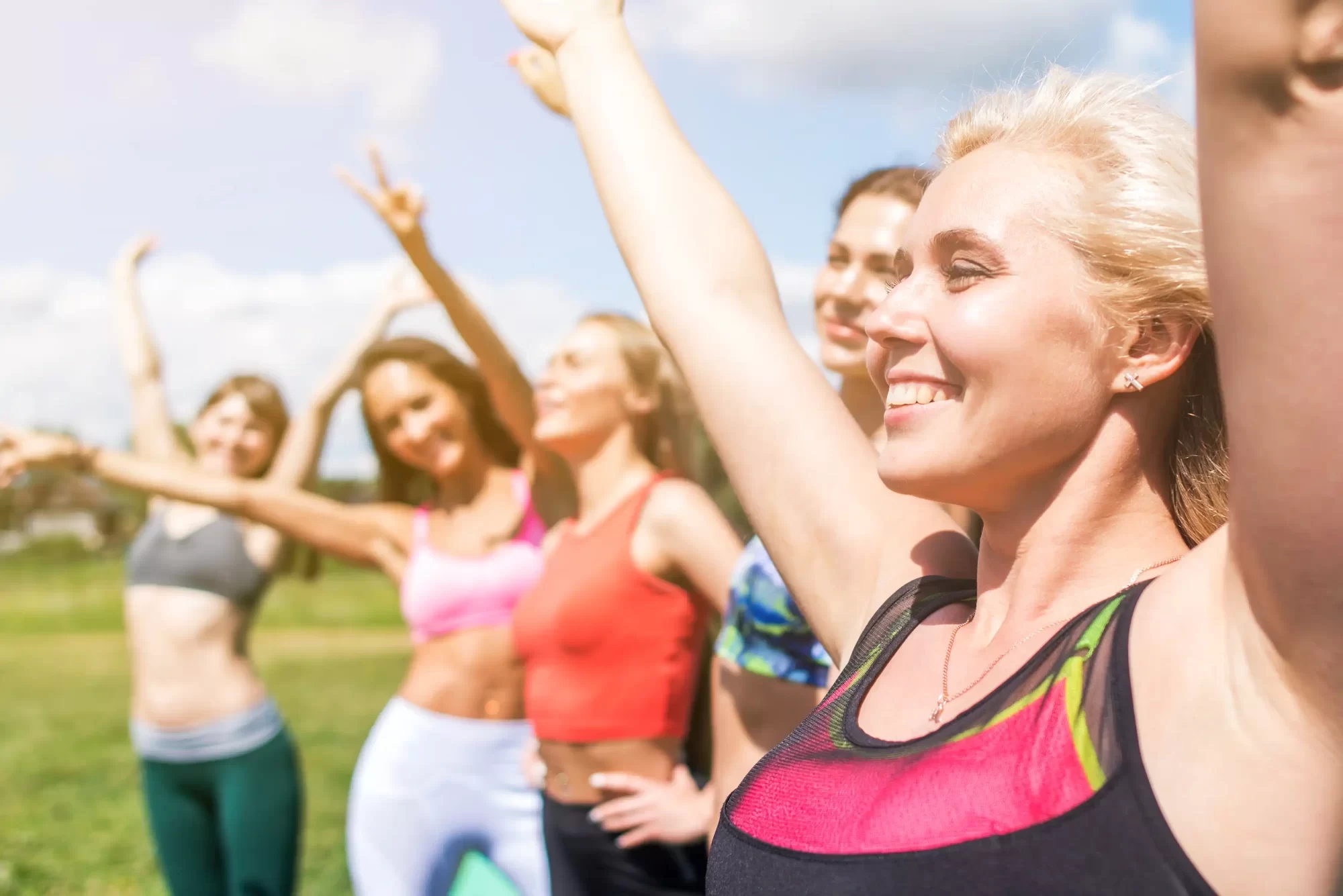 Donne che fanno esercizi all'aperto sorridendo sotto il sole.