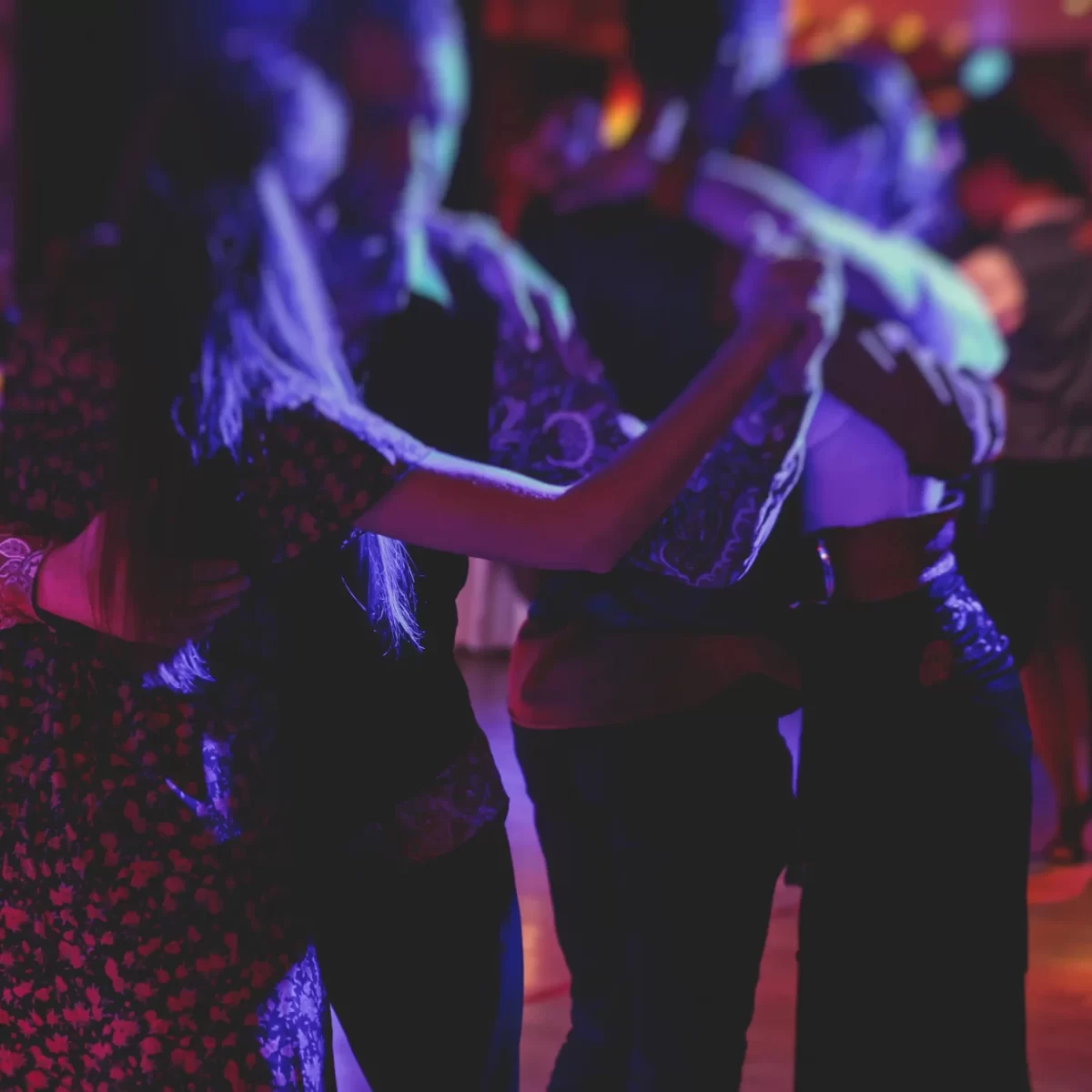 Persone che ballano in coppia in una sala con illuminazione soffusa e colorata.