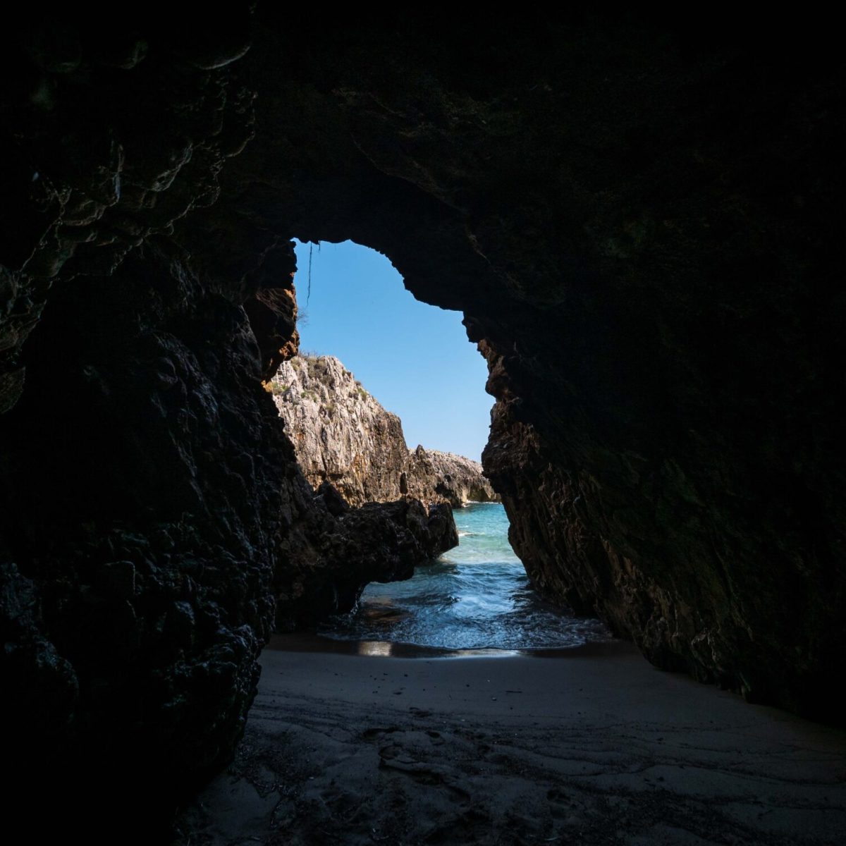 Vista di un'uscita di grotta verso il mare con cielo blu.