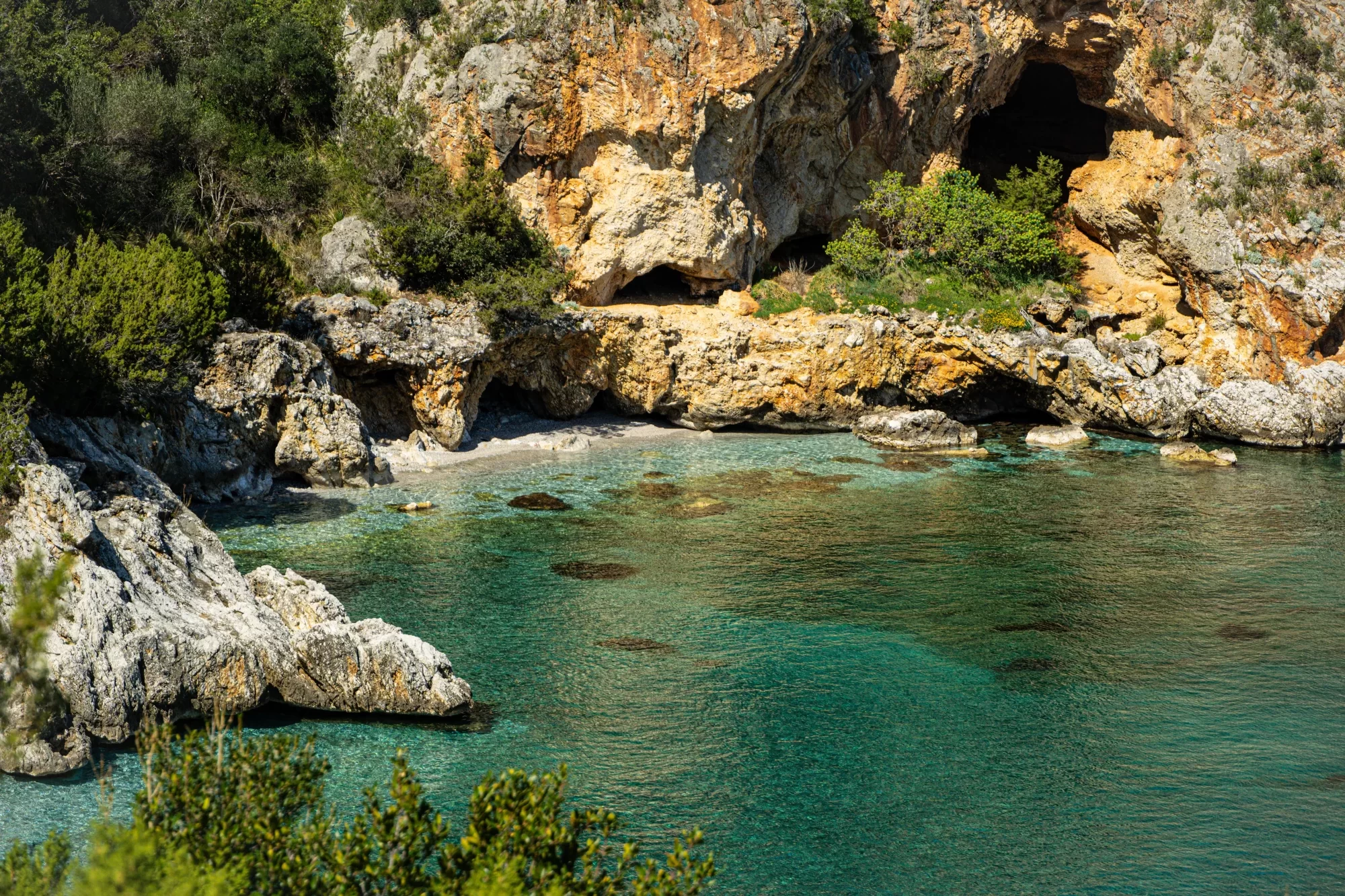 Baia rocciosa con mare turchese e vegetazione mediterranea.