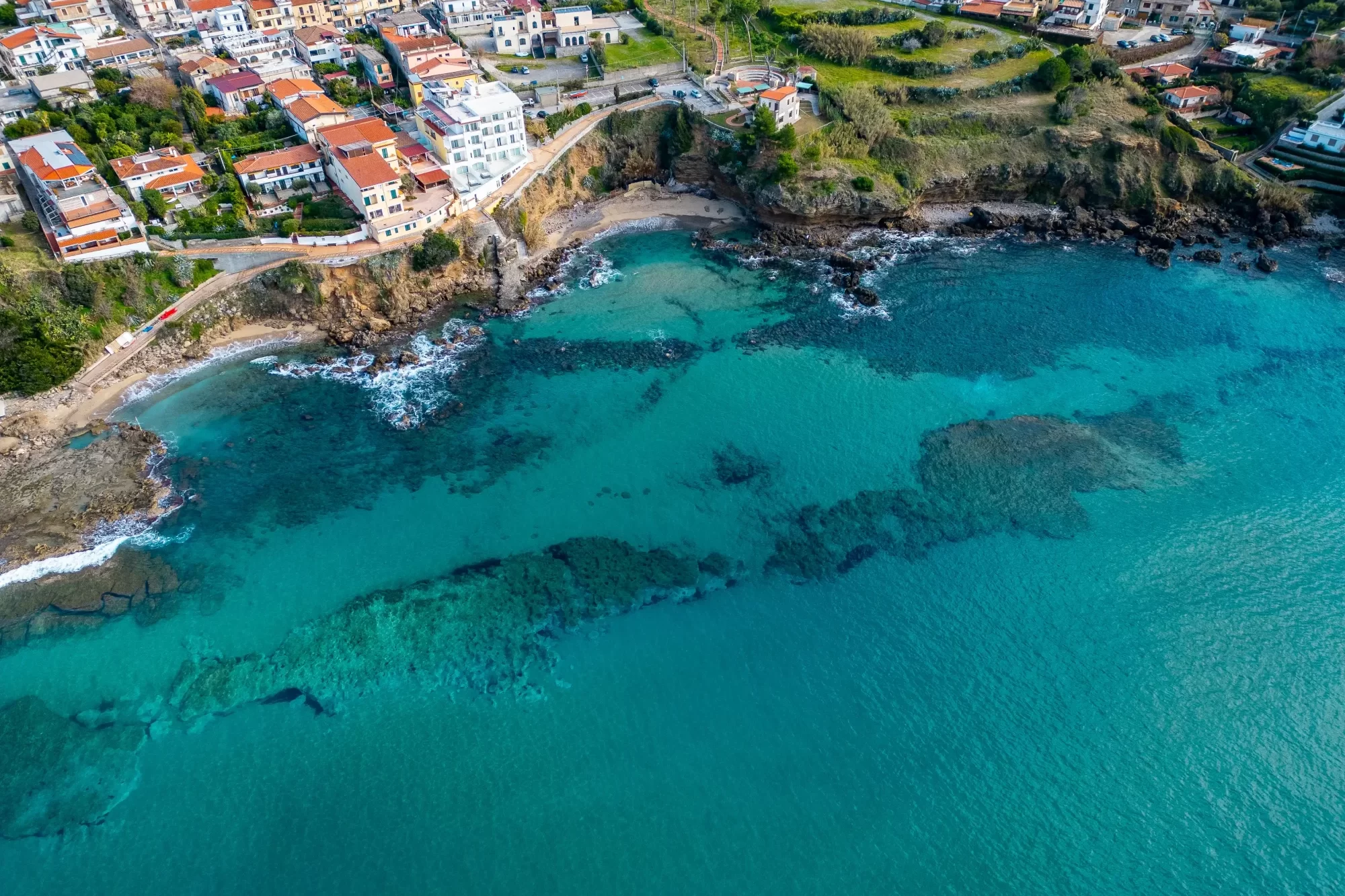 Veduta aerea di una costa con acque turchesi e un villaggio colorato.