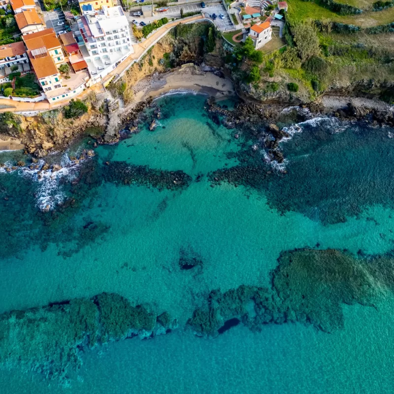 Vista aerea di una costa rocciosa con acque turchesi e costruzioni residenziali lungo la riva.
