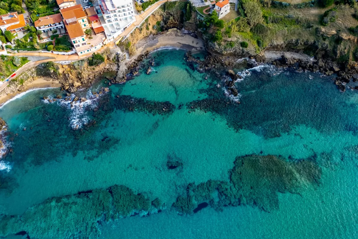 Vista aerea di una costa rocciosa con acque turchesi e costruzioni residenziali lungo la riva.