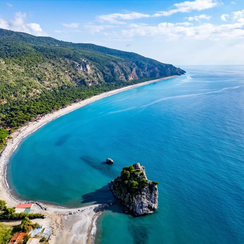 Spiaggia e mare cristallino circondati da una rigogliosa vegetazione collinare.