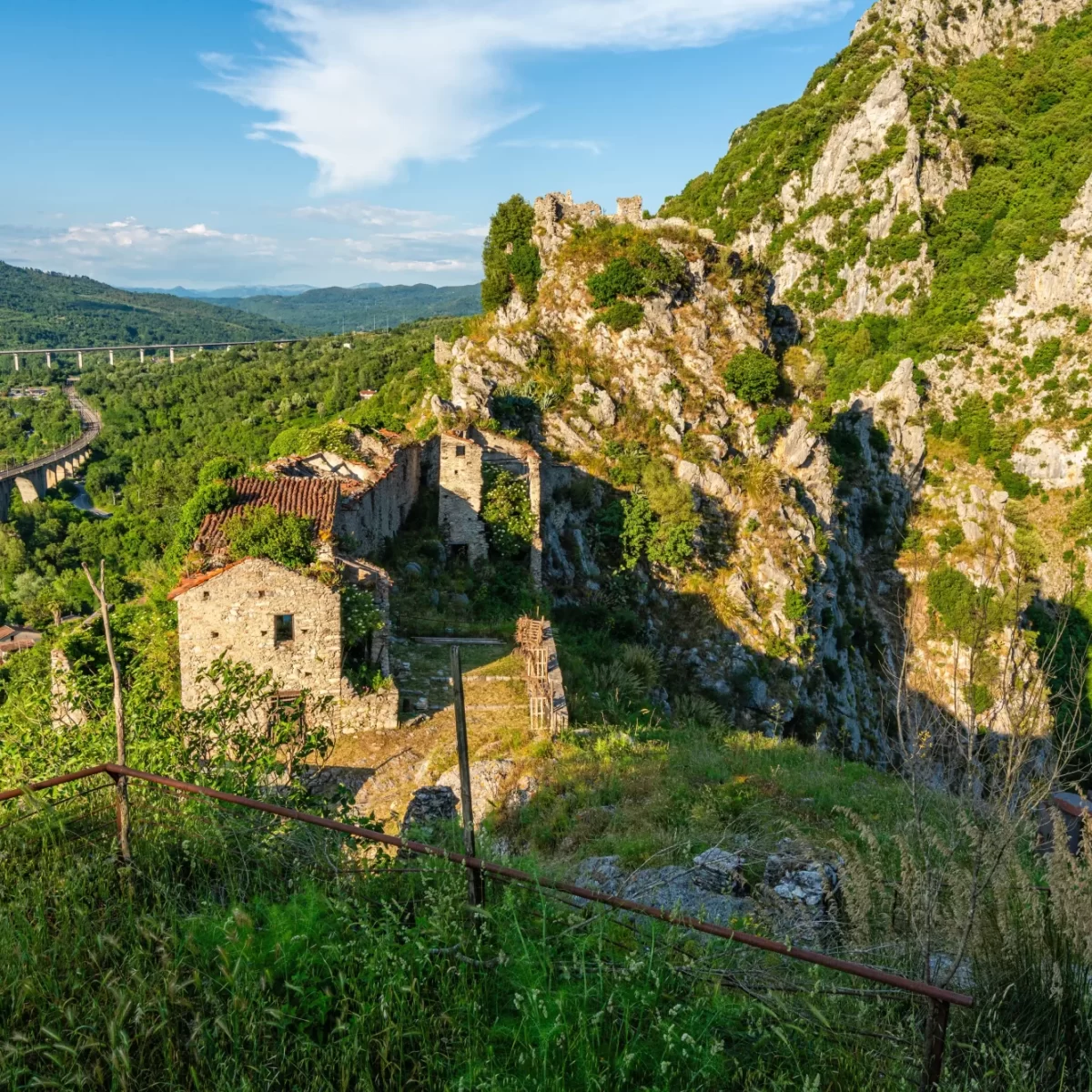Paesaggio montano con ruderi di edifici e un ponte in lontananza.