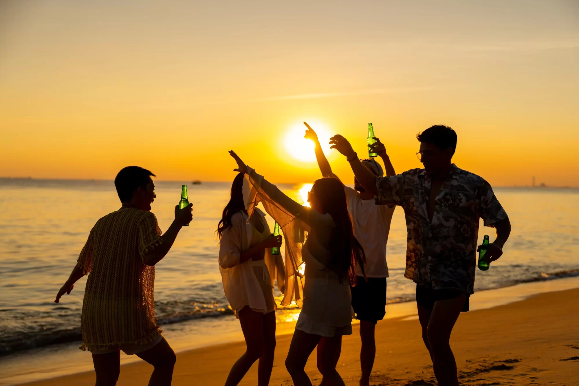 Persone che ballano e si divertono al tramonto sulla spiaggia.