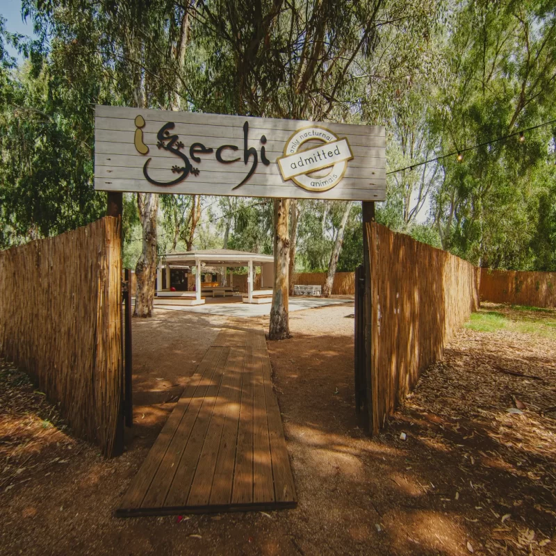 Ingresso di un'area naturale recintata con un cartello che dice "I Gechi", circondata da alberi e vegetazione.