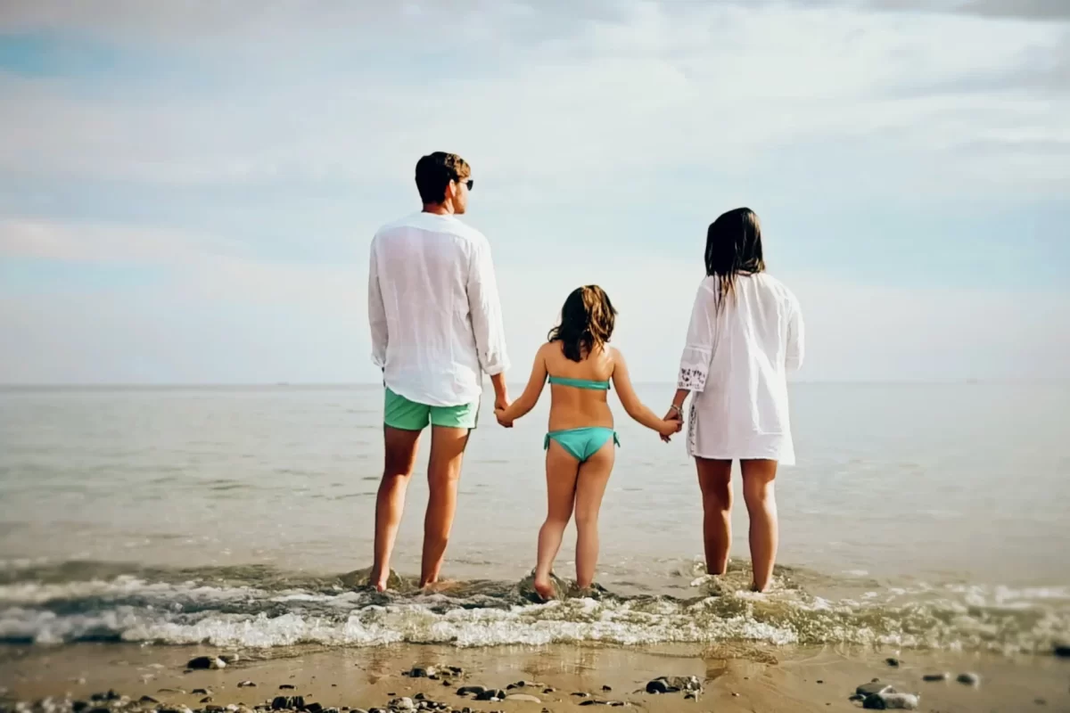Una famiglia vista di spalle, mano nella mano, sulla riva del mare.