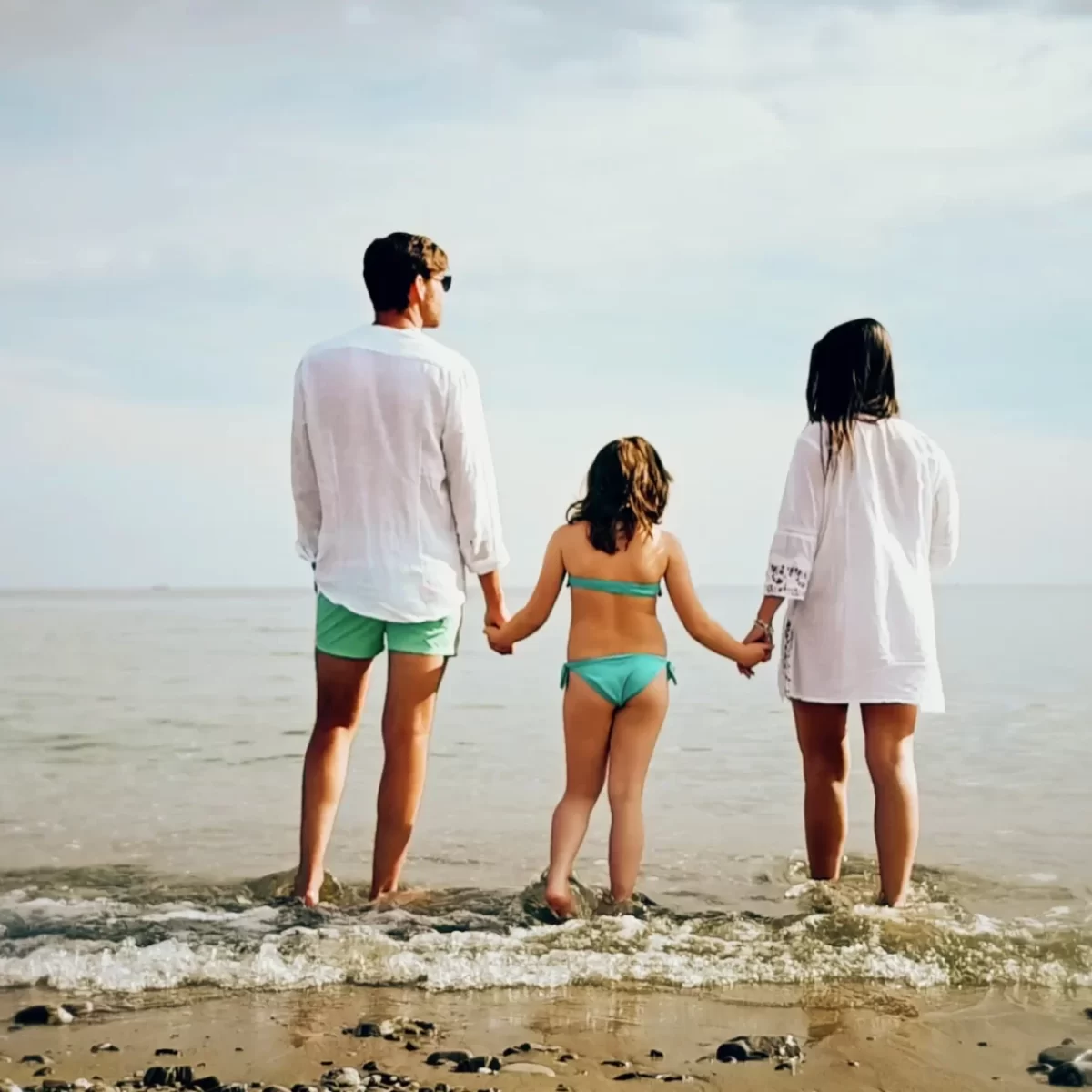 Una famiglia vista di spalle, mano nella mano, sulla riva del mare.