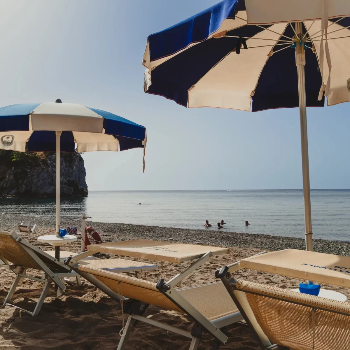 Spiaggia con lettini e ombrelloni vicino al mare calmo con un promontorio sullo sfondo.