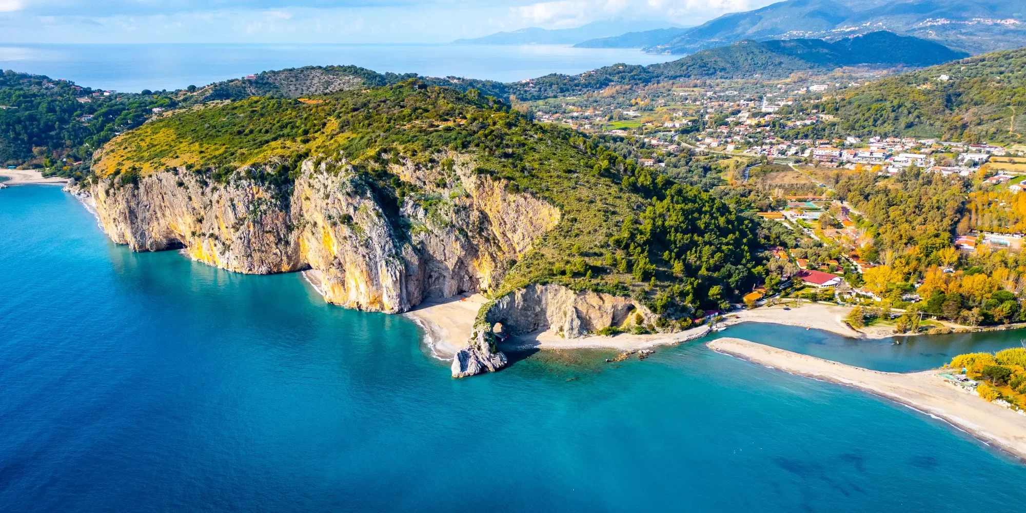 Veduta aerea di una costa rocciosa con spiagge e mare blu circondata da verdeggianti colline.