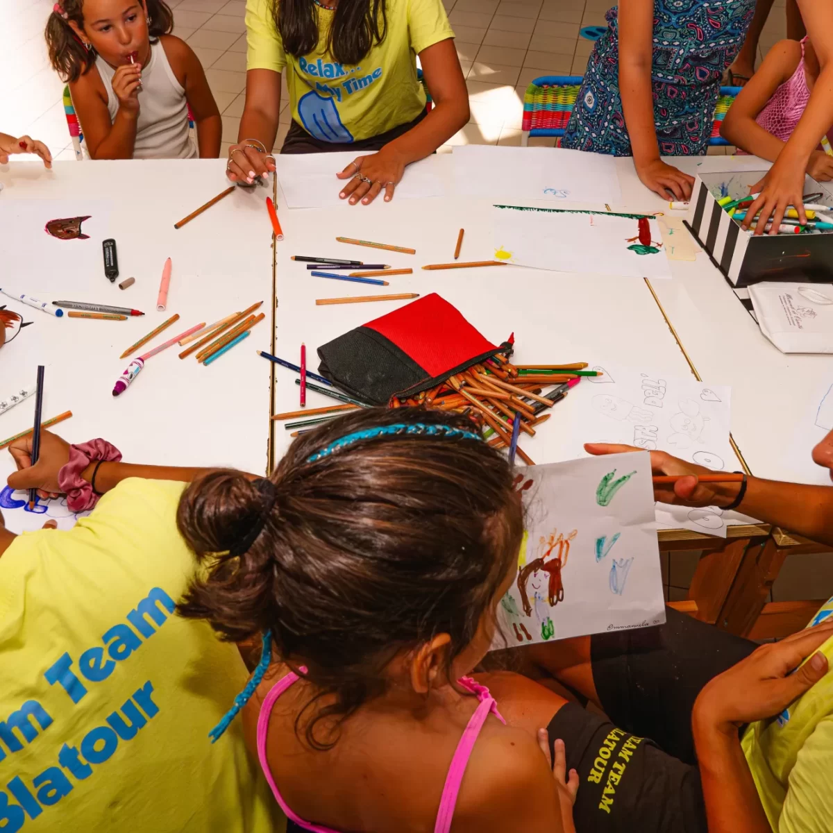 Bambini e adulti disegnano insieme a un tavolo pieno di matite colorate.
