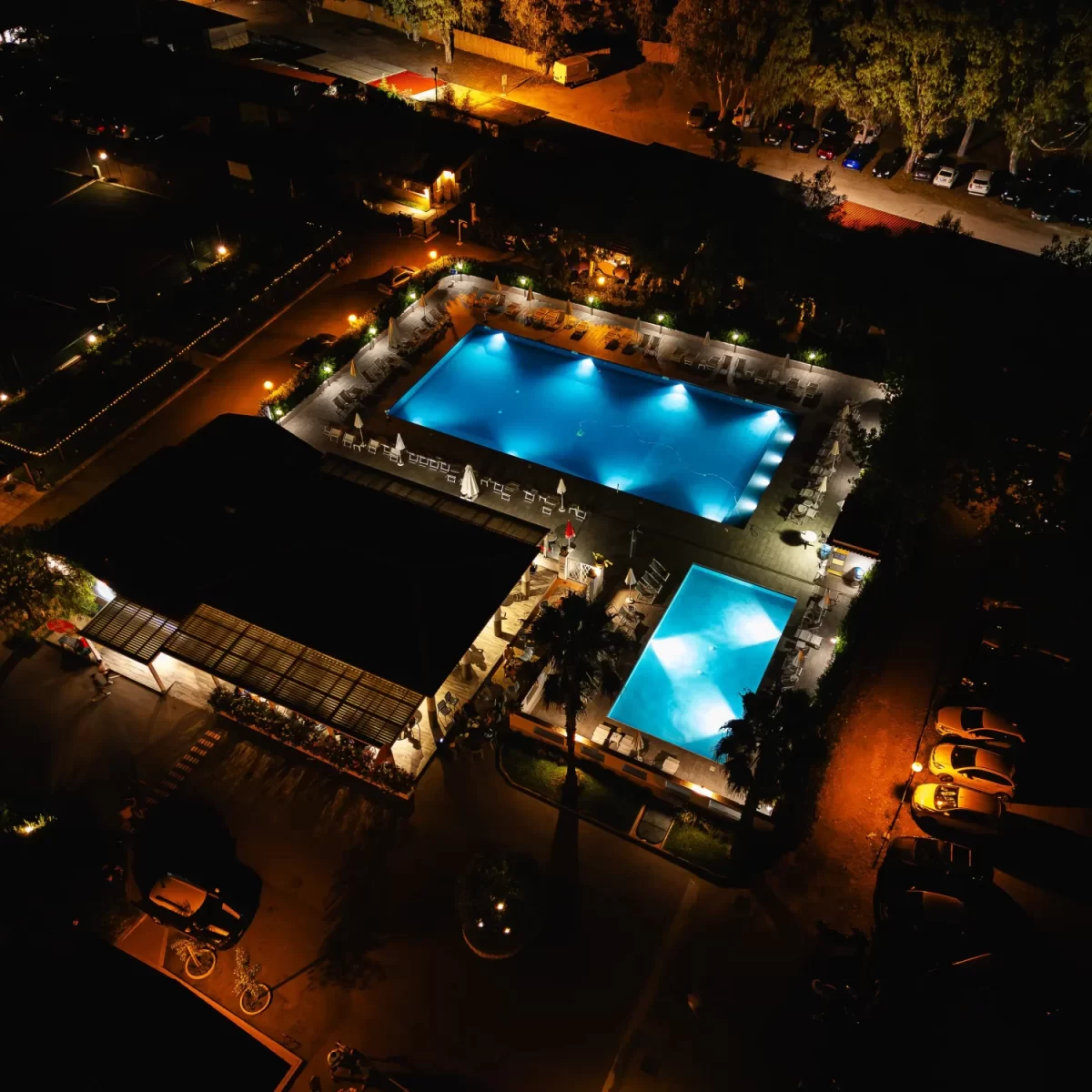 Veduta aerea notturna di una zona con piscine illuminate e area ricreativa.