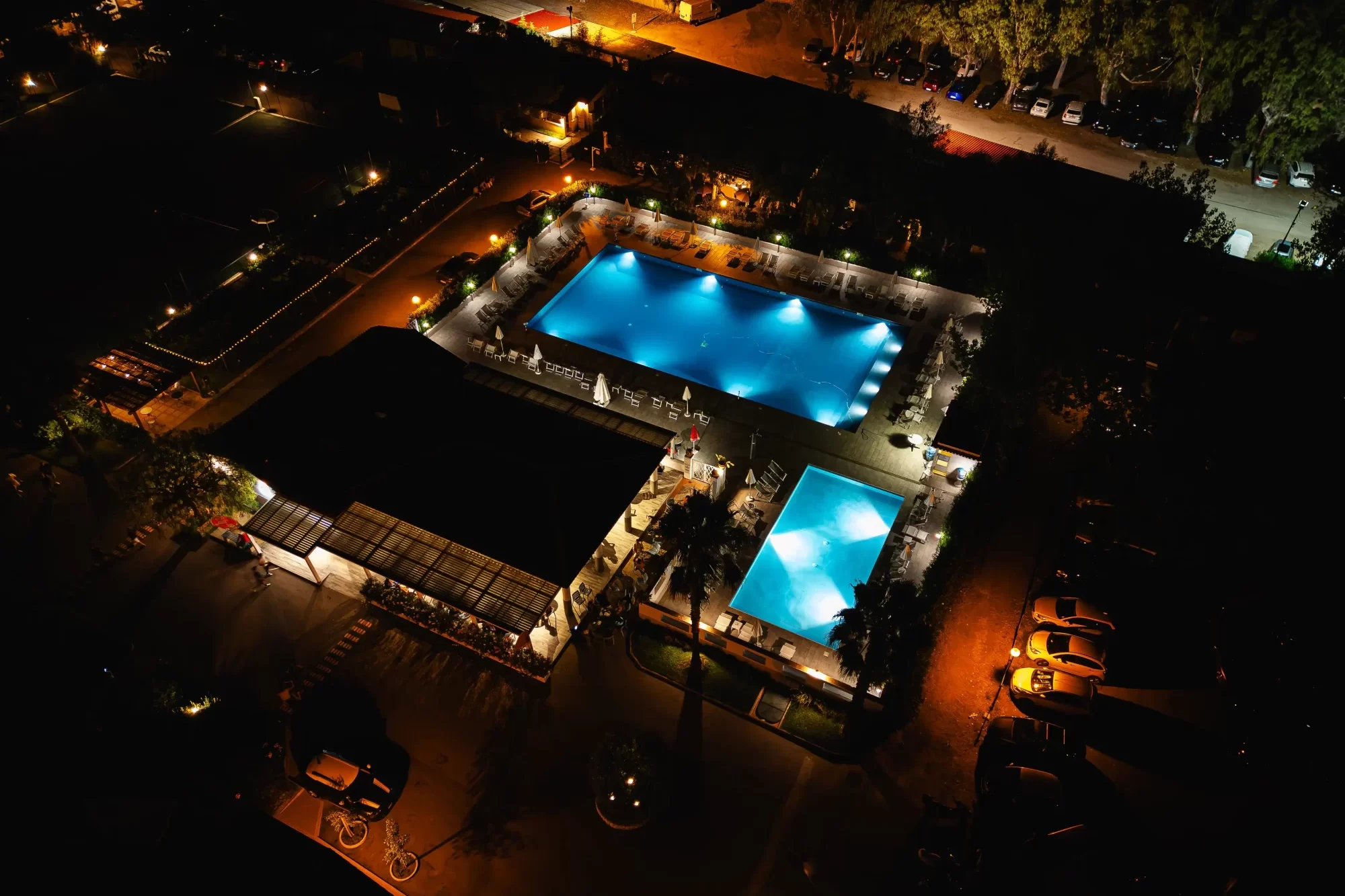 Veduta aerea notturna di una zona con piscine illuminate e area ricreativa.