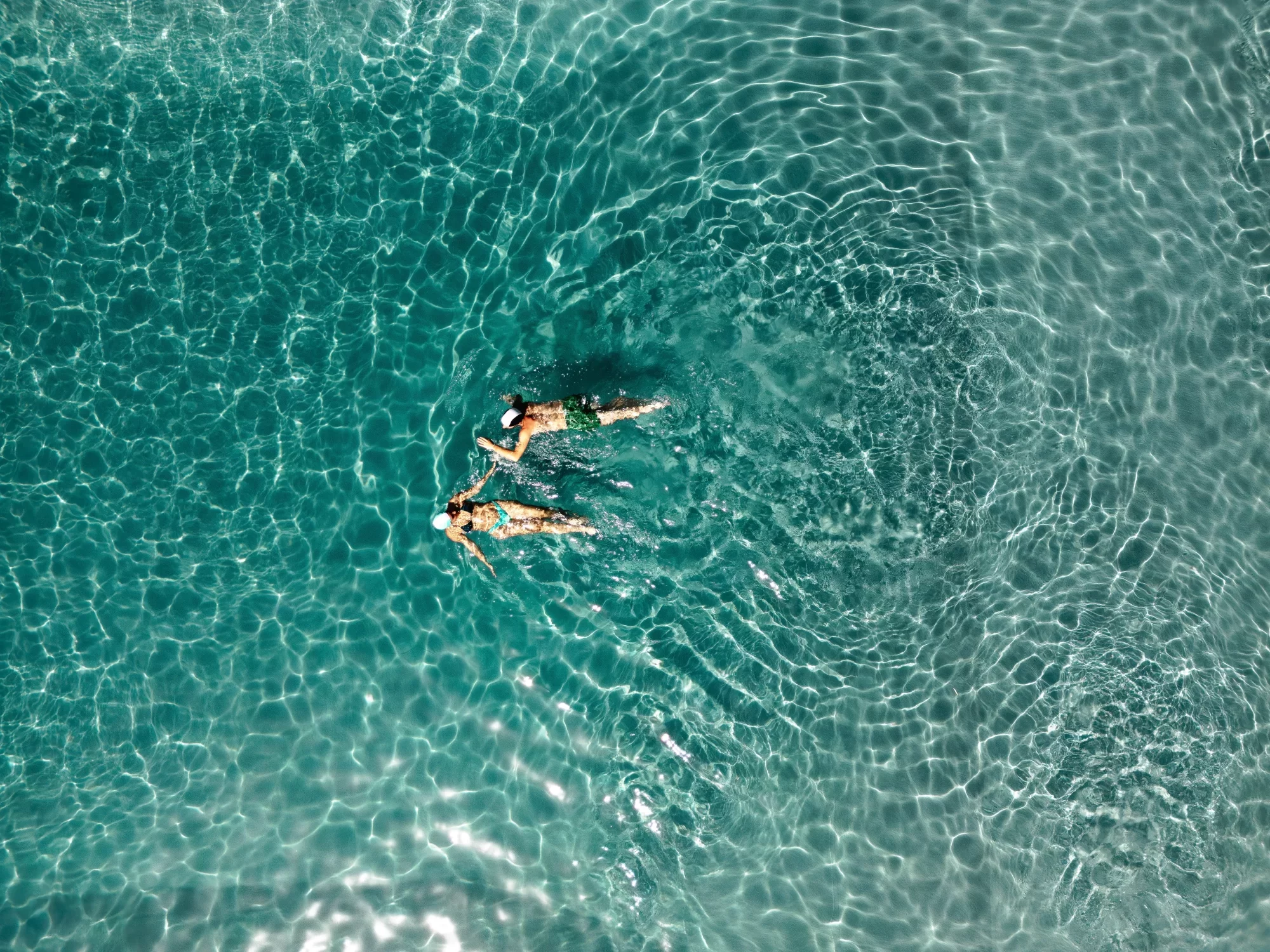 Due persone nuotano in un mare limpido visto dall'alto.