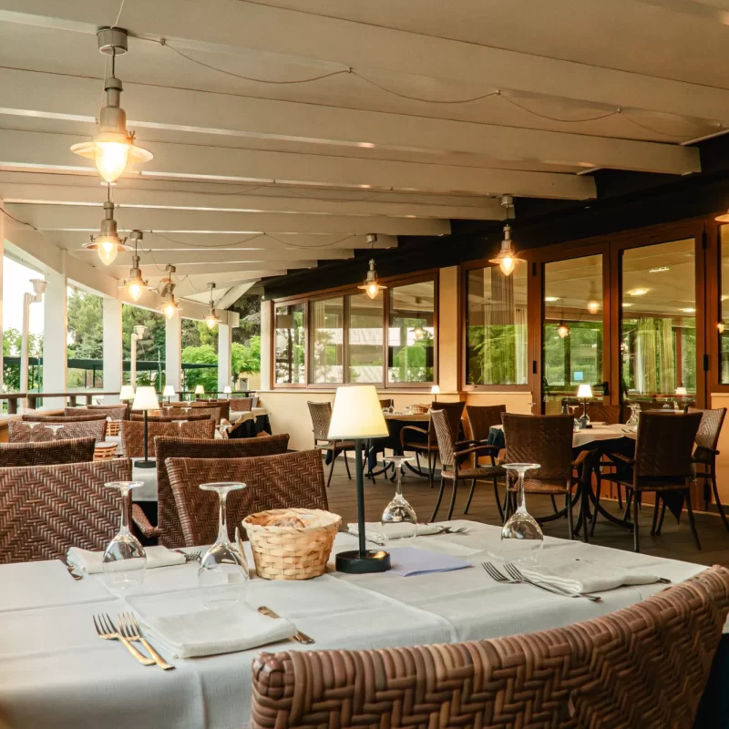 Terrazza di un ristorante all'aperto con tavoli apparecchiati e sedie in vimini.