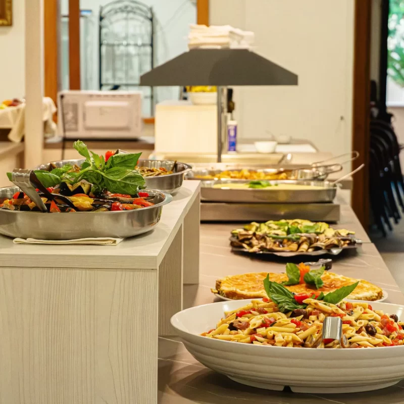 Buffet con piatti di pasta e verdure in un ambiente luminoso.