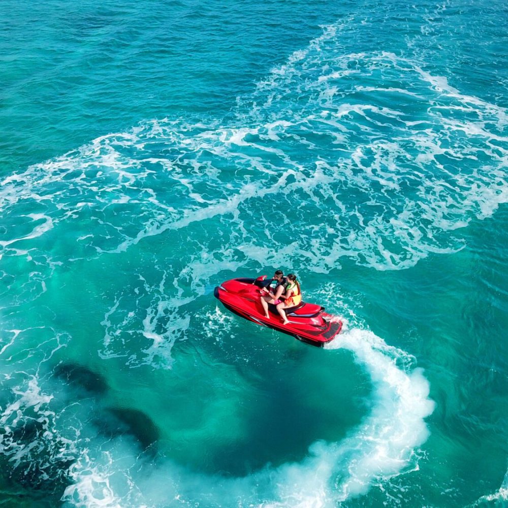 Due persone su una moto d'acqua rossa sfrecciano su un mare turchese.