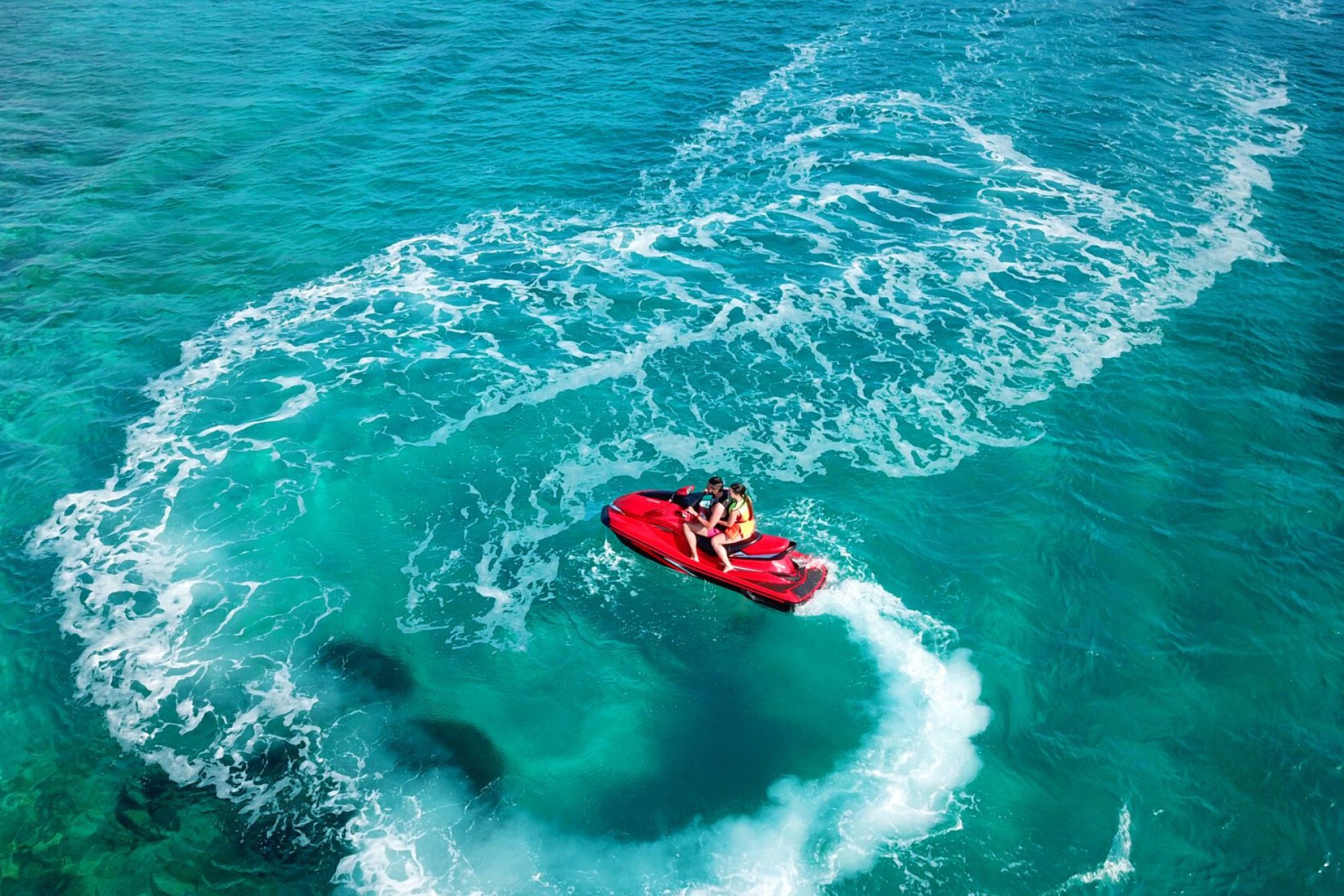 Due persone su una moto d'acqua rossa sfrecciano su un mare turchese.