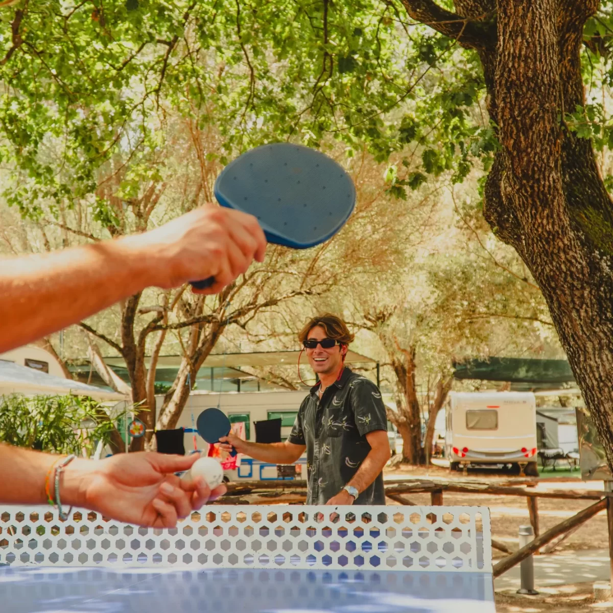 Persone giocano a ping-pong all'aperto in una giornata soleggiata.