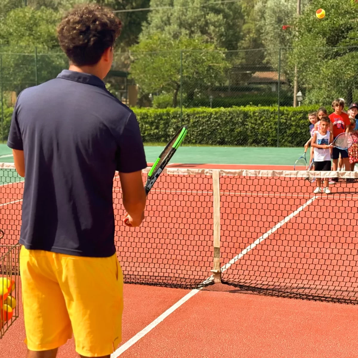Maestro di tennis insegna a un gruppo di bambini su un campo all'aperto.