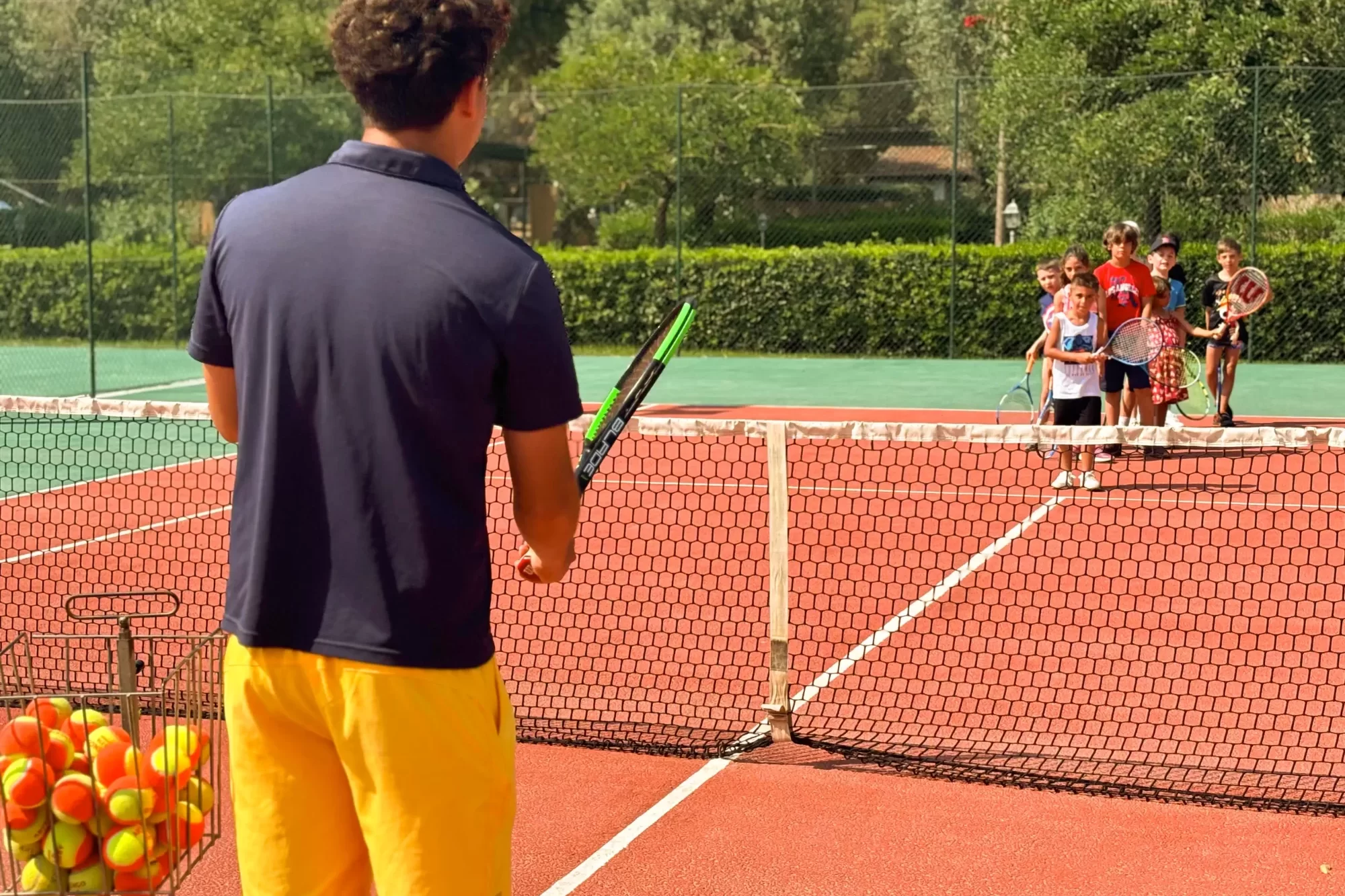 Maestro di tennis insegna a un gruppo di bambini su un campo all'aperto.