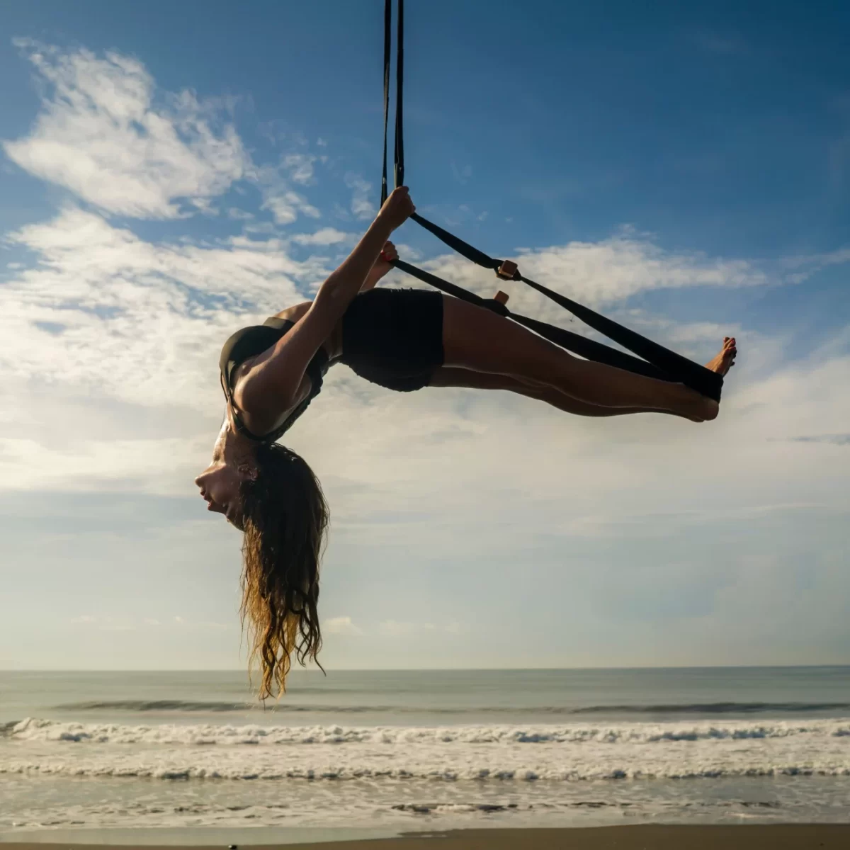 Persona che pratica yoga aereo sulla spiaggia con il mare sullo sfondo.